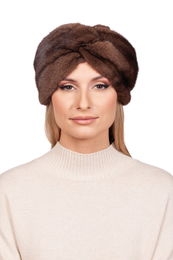 A woman with long blonde hair is wearing a beige cashmere sweater and the FurbySD Brown Mink Fur Turban Hat With Cashmere Top, which covers her ears. She has a neutral expression and is facing the camera against a white background.