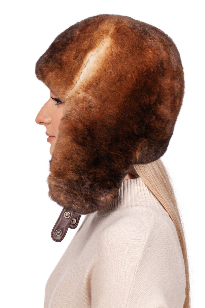 Side profile of a person wearing a brown rabbit fur ushanka hat with ear flaps and a beige sweater against a white background.