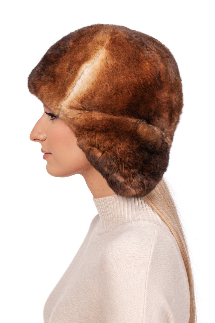 Side profile of a woman wearing a luxurious brown rex rabbit fur trooper hat, showcasing winter fashion accessories. The woman is dressed in a cream-colored turtleneck sweater, highlighting a cozy winter style.