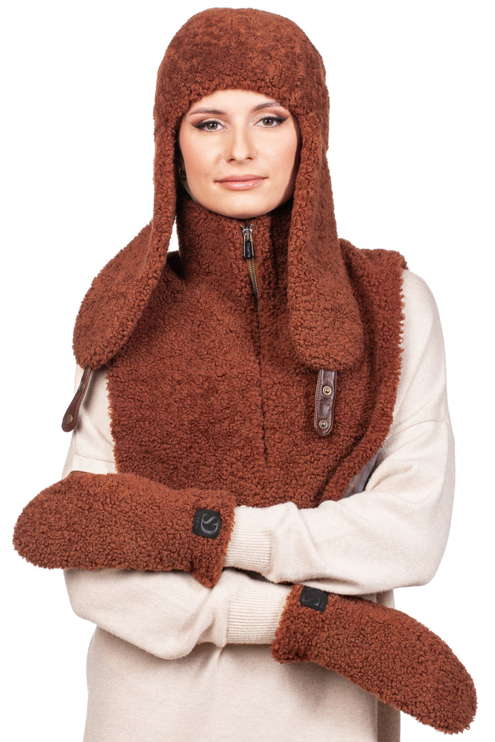 A person wearing the cozy Brown Shearling Fur Accessories Set from FurbySD, complete with a hat featuring long ear flaps, a matching collar, and mittens, showcases the essence of winter accessories. With arms crossed over a light-colored sweater and a soft smile, they embody the understated elegance of luxury fashion.