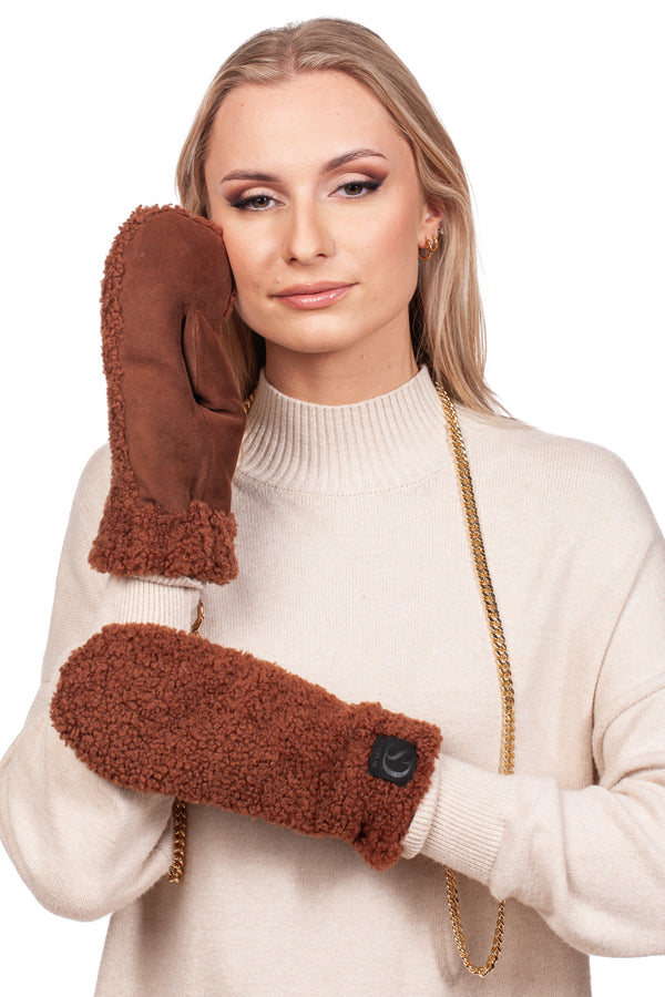 A person with long hair wearing a cream sweater holds one of the Brown Shearling Fur Mittens With Detachable Chain by FurbySD to their face, while the other hand wears its match. A detachable gold chain elegantly adorns their neck, and the handmade mittens stand out against the plain white background.