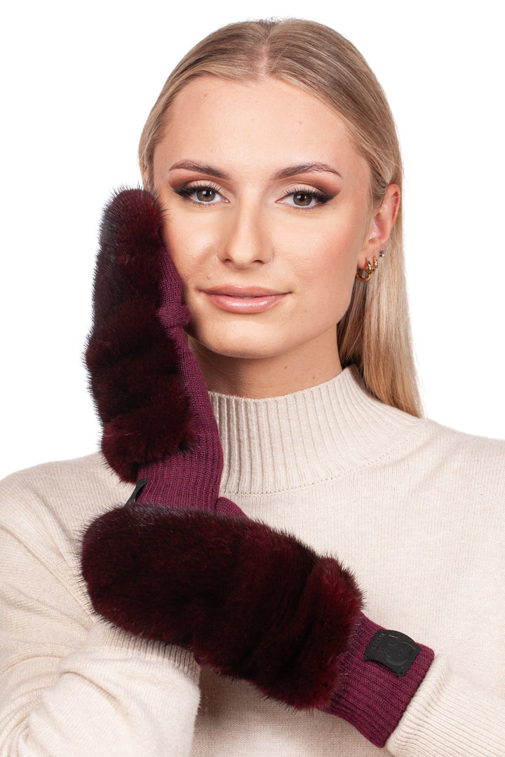 A woman in a cream turtleneck sweater is wearing FurbySD Burgundy Red Mink Fur Flip Top Mittens, crafted with genuine mink fur. She smiles softly, one gloved hand touching her face, while her blond hair falls straight against the plain white background.