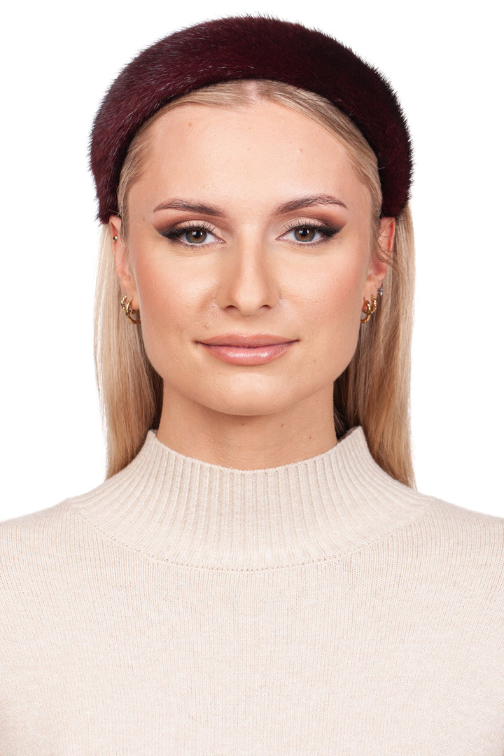 A woman with long blonde hair poses elegantly against a plain white background, wearing a FurbySD Burgundy Red Mink Fur Hairband and a beige turtleneck sweater. She complements her look with subtle makeup and small hoop earrings.