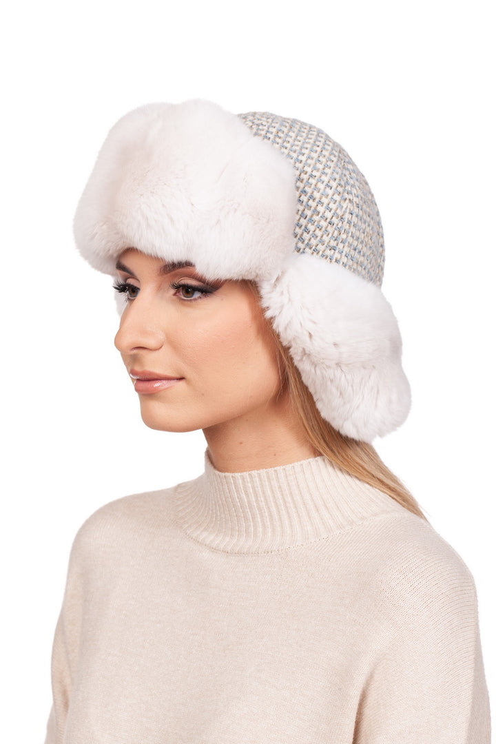 A person is wearing the Cream White Chinchilla Fur Ushanka Hat by FurbySD, featuring a luxurious design with houndstooth patterns and white faux fur trim, paired with a light beige turtleneck sweater against a white background.