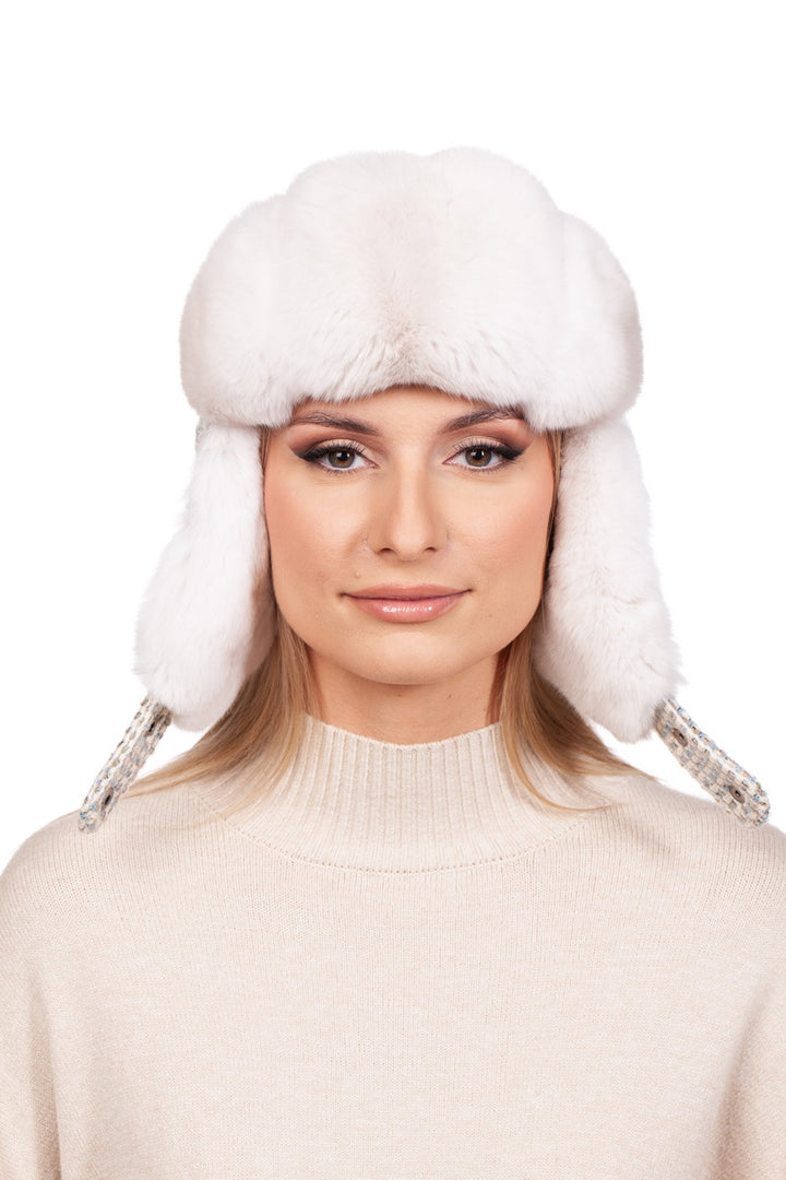 A person wearing a luxurious Cream White Chinchilla Fur Ushanka Hat by FurbySD, along with a light beige sweater, is looking at the camera against a plain white background.