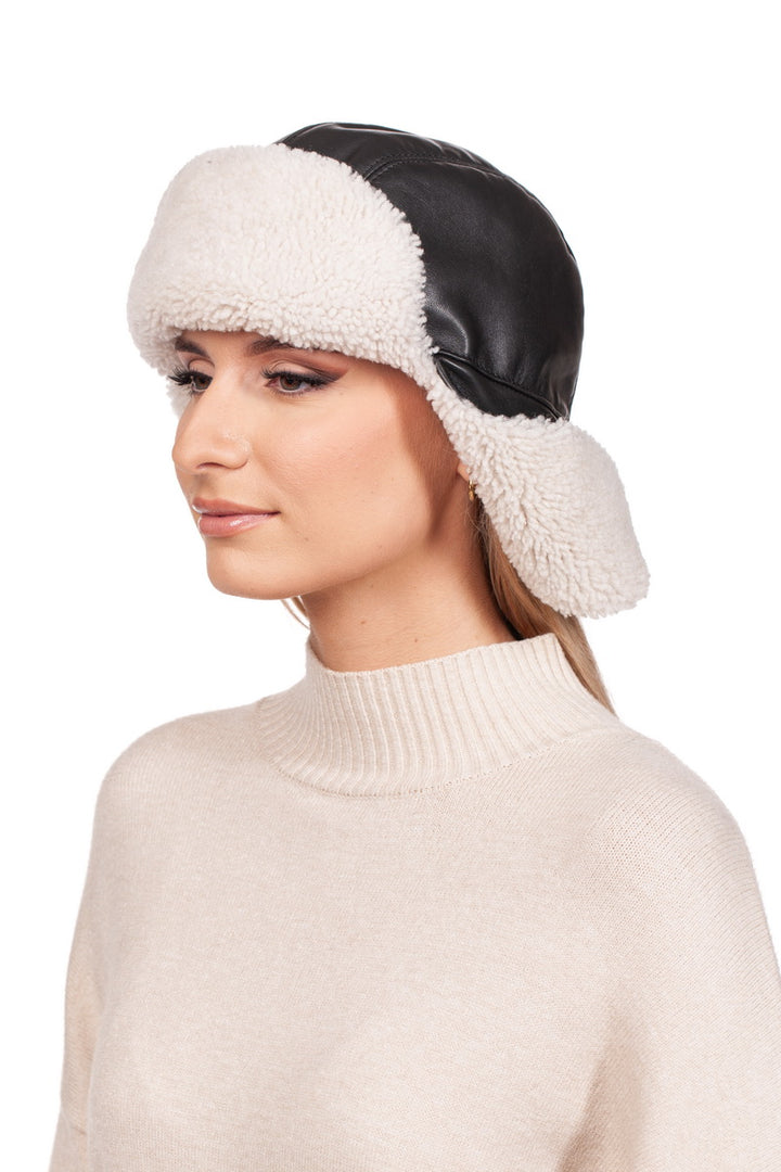 A person in a cream-colored turtleneck sweater and a stylish FurbySD White Shearling Fur Aviator Bomber Hat crafted from black Nappa leather with white shearling fur covering their ears, gazes to the side against a white background.