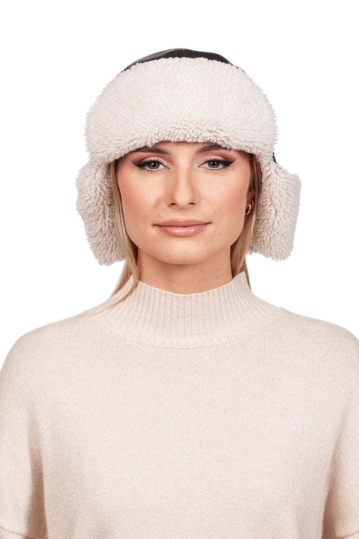 A person, dressed in a fluffy ear warmer and a cream-colored sweater, smiles slightly as their elegant touch is enhanced by the FurbySD White Shearling Fur Aviator Bomber Hat against the white background.