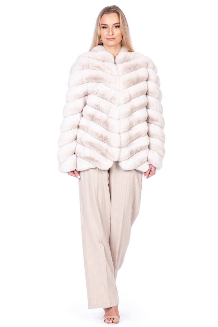 A person in a luxurious FurbySD Cream Chinchilla Fur Coat and beige wide-legged trousers stands smiling against a plain white backdrop.