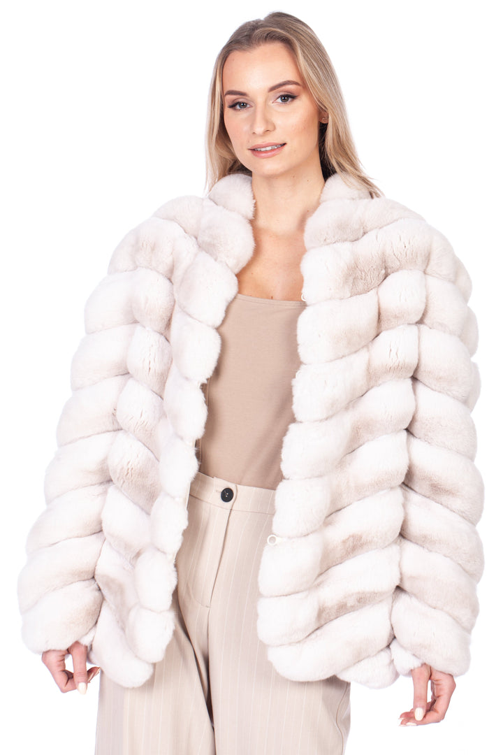 Standing elegantly against a pristine white background, a woman drapes the luxurious "Cream Chinchilla Fur Coat" by FurbySD over her beige top and light-colored pants.