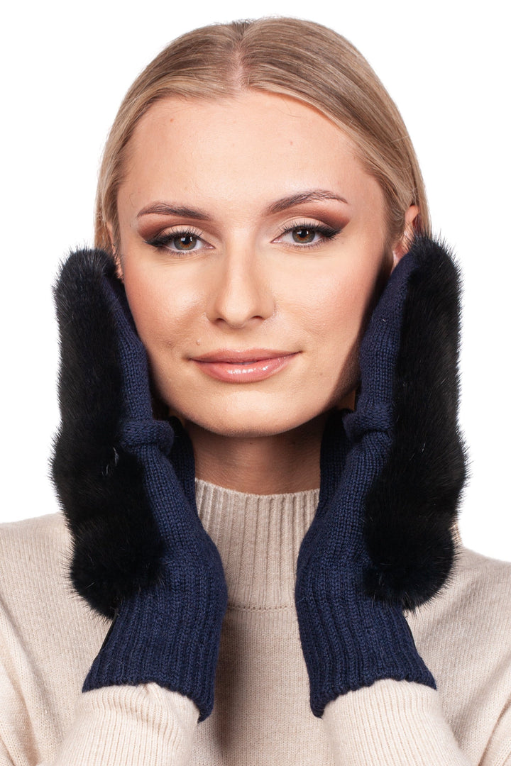 A blonde-haired woman smiles while wearing Dark Blue Mink Fur Flip Top Mittens by FurbySD, which are elaborately designed with a black fur trim. The background is plain white.