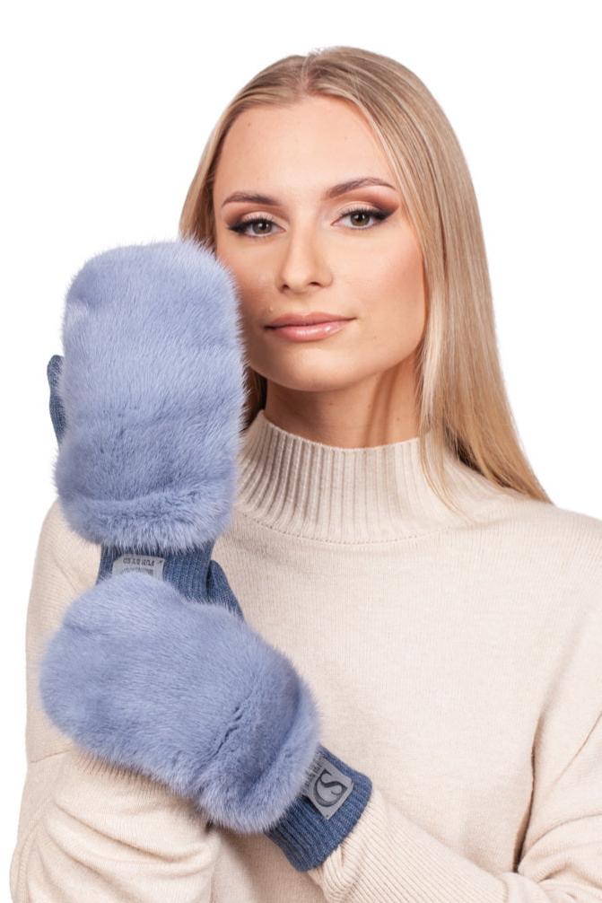 A person with long blonde hair wearing a light beige sweater holds up FurbySD's luxurious Denim Blue Mink Fur Flip Top Mittens to their face. The cozy, plush appearance of the mittens complements their gentle expression as they gaze directly at the viewer.