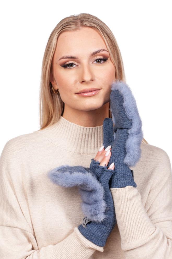 A woman with long blonde hair is wearing a beige sweater and stylish Denim Blue Mink Fur Flip Top Mittens from FurbySD. She poses elegantly with her hand near her face against a white background, exuding warmth and style.