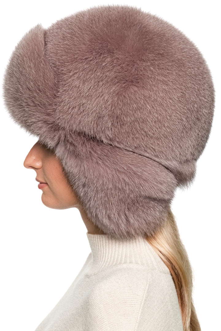 Profile view of women’s dusty pink fox fur trapper hat, thick plush fur with earflaps down, oversized ushanka style winter hat for après-ski elegance.