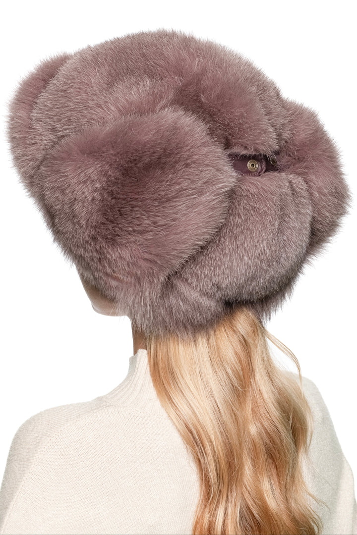 Side angled portrait of woman wearing dusty pink fox fur trapper hat, fluffy ushanka with voluminous crown and ear warmers for après-ski style.