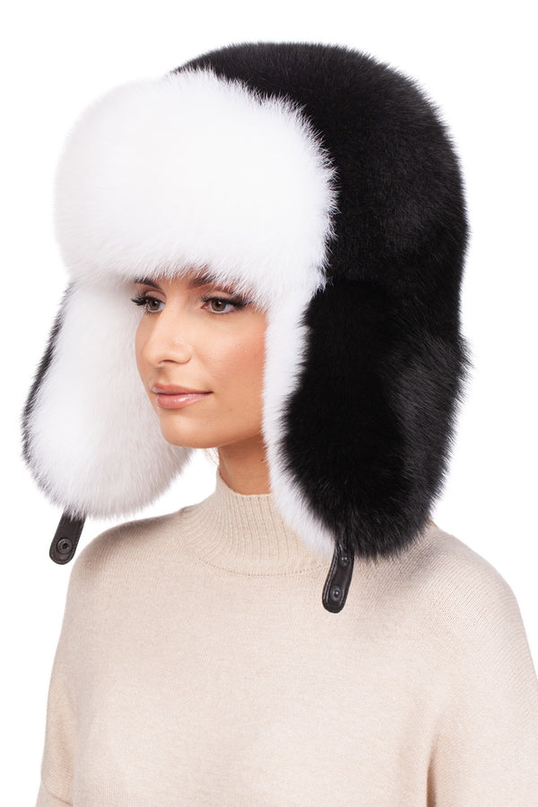 Sporting the Fox Fur Ushanka Trapper Hat by FurbySD, a person stands against a plain white background, complete with its large, fluffy black and white fox fur and dangling ear flaps. They pair it stylishly with a beige sweater.