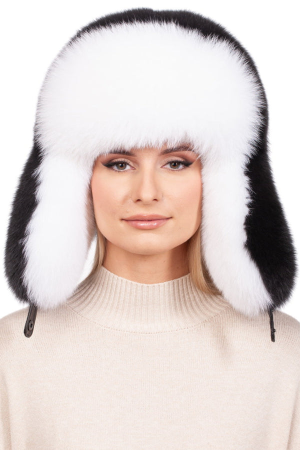 A person wears a beige sweater and the classic winter essential: a white and black Fox Fur Ushanka Trapper Hat by FurbySD, complete with ear flaps. The plain white background enhances the cozy vibe.