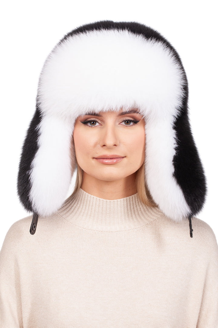 A person wears a beige sweater and the classic winter essential: a white and black Fox Fur Ushanka Trapper Hat by FurbySD, complete with ear flaps. The plain white background enhances the cozy vibe.