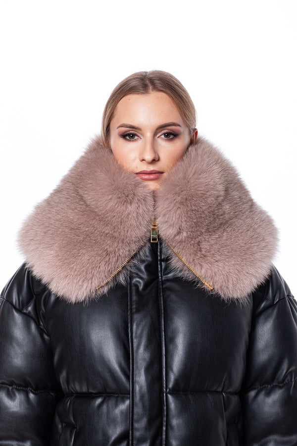 A person is wearing a black leather puffer jacket adorned with a luxurious FurbySD Fox Fur Zipped Collar Scarf, featuring a large, plush, light brown fur that doubles as an elegant neck warmer. The plain white background enhances the striking contrast between the jacket and the fur collar. The individual has light hair pulled back.