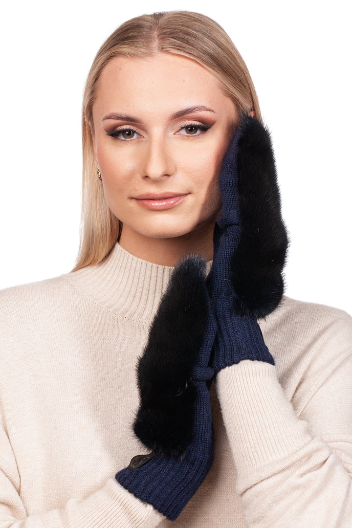 A person with long blonde hair is wearing a beige sweater and FurbySD's Dark Blue Mink Fur Flip Top Mittens. They gently touch their face with both hands, smiling subtly against a plain background. The luxurious mittens from FurbySD add an exquisite touch to the serene scene.