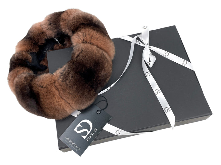 A luxurious brown chinchilla fur headband, crafted from premium quality fur, is elegantly placed on a dark grey gift box tied with a white ribbon imprinted with an "S" logo. A tag attached to the headband reads "Genuine Camo, Furtivity by FurbySD.