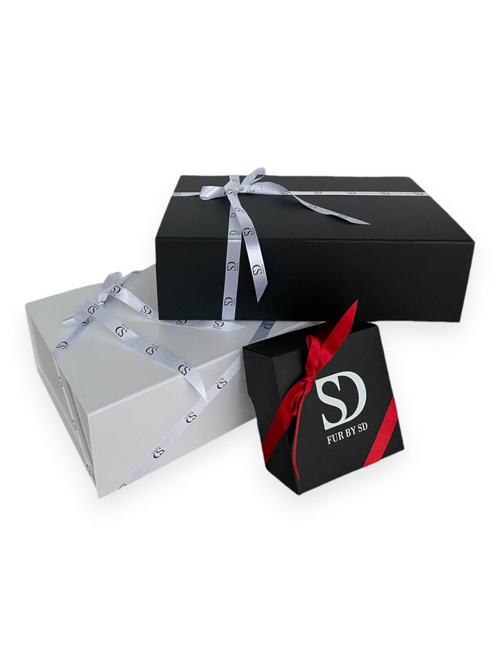 Three gift boxes are stacked elegantly. The largest box is black with a white ribbon, the medium one is white with a patterned ribbon, and the smallest is black with a red ribbon featuring the "FurbySD" logo. Inside, you'll find exquisite Pearl Mink Fur Flip Top Mittens that promise both luxury and warmth.