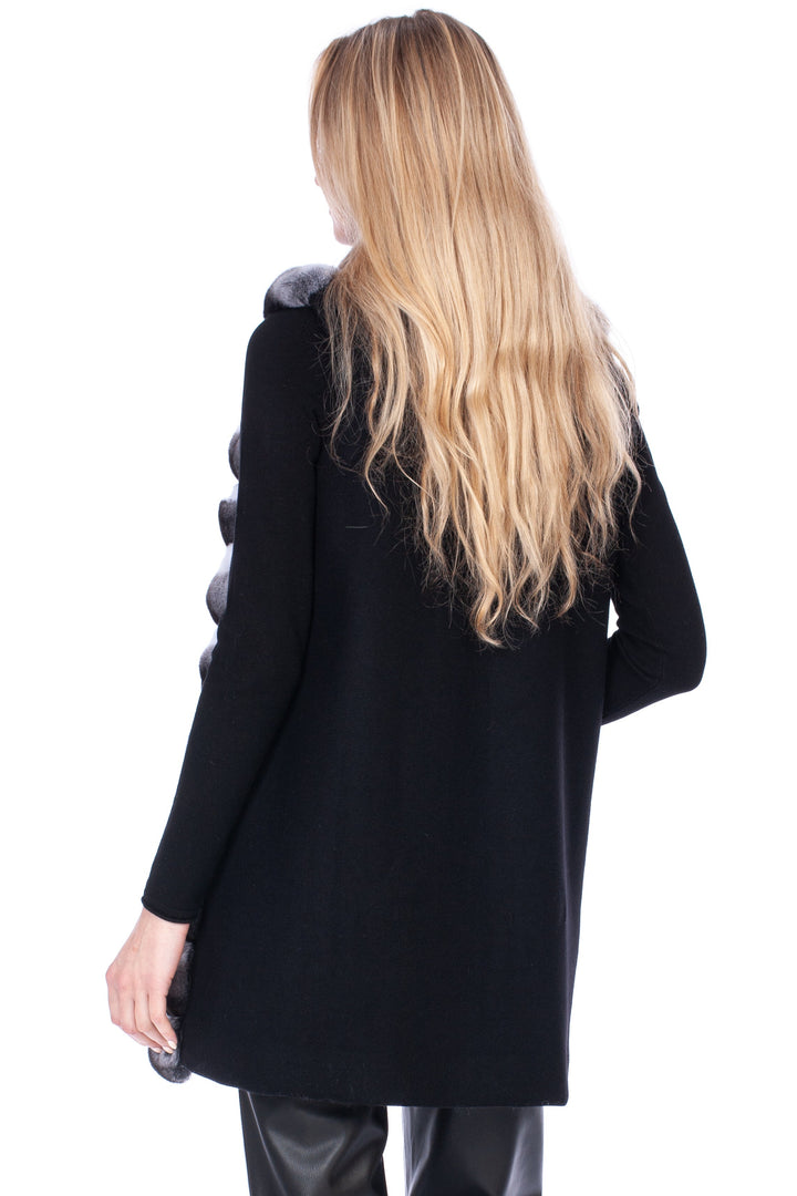 Person wearing a black wool coat with chinchilla fur trim on front of it and black pants on a white background.