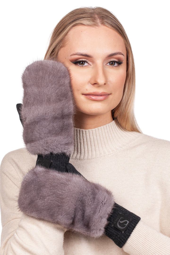 An individual wearing a cozy cream sweater poses with FurbySD's luxurious Grey Mink Fur Headband and Mittens. One mitten, crafted from plush silverblue mink fur, is held up to their face as they gently smile, perfectly embodying the essence of luxury winter accessories.