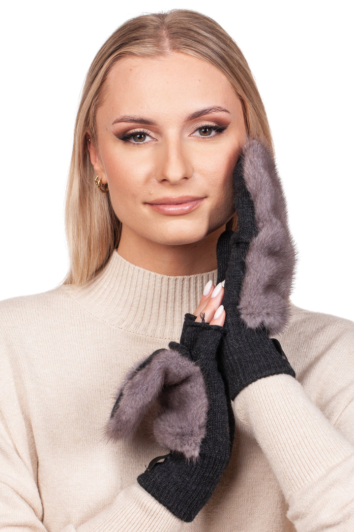 A woman with long blonde hair is wearing a beige sweater and elegantly cups her face using FurbySD's luxurious black mittens with distinctive silverblue mink fur accents. Her gentle smile is set against a simple white backdrop, embodying the essence of sophisticated winter accessories.