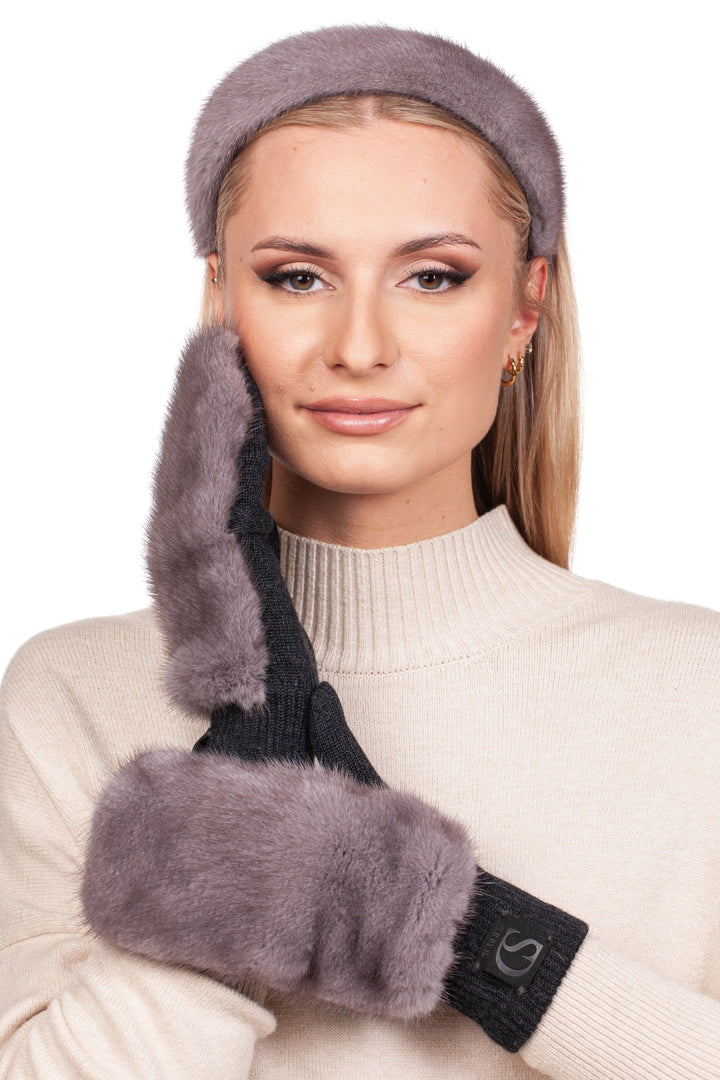 A person with long blonde hair wears a beige turtleneck sweater and a luxurious Grey Mink Fur Headband and Mittens by FurbySD. They pose against a plain white background, gently touching their cheek with one hand.