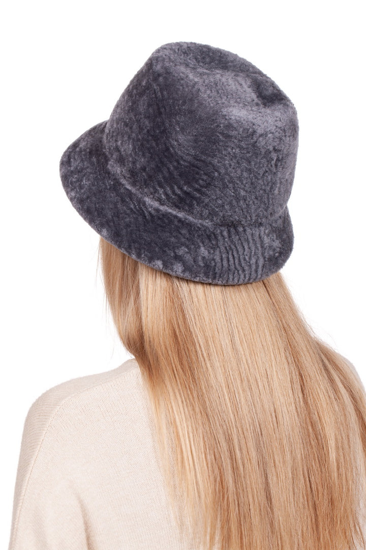 A person with long blonde hair is wearing a Grey Sheepskin Bucket Hat from FurbySD, characterized by its soft texture and flexible brim. They face away, displaying the back of their head and shoulders while wearing a light beige top against a plain white background.