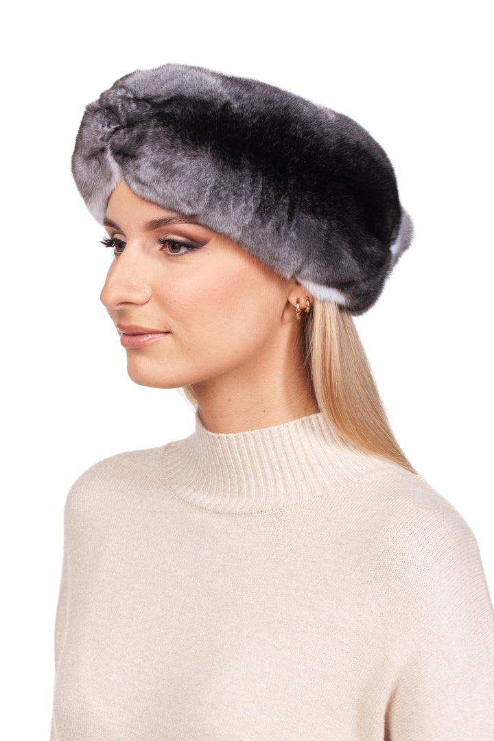 A woman with long blonde hair is wearing the luxurious Twisted Chinchilla Fur Headband by FurbySD, which beautifully accents her cream-colored turtleneck sweater. Her subtle eye makeup completes her elegant winter look as she gazes to her right against a plain white background.