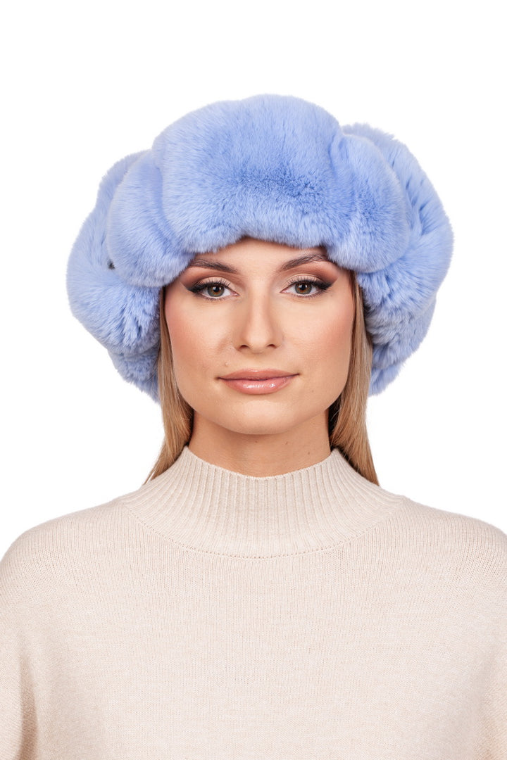 A person wearing a Blue Chinchilla Fur Ushanka Hat by FurbySD and a cream-colored sweater looks directly at the camera with a neutral expression against a plain white background.