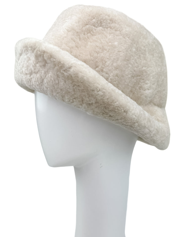 The Pearl White Astrakhan Fur Bucket Hat by FurbySD is displayed on a white mannequin head. This hat features a wide, soft brim and a fluffy texture, offering a cozy and luxurious appearance reminiscent of plush Astrakhan fur.