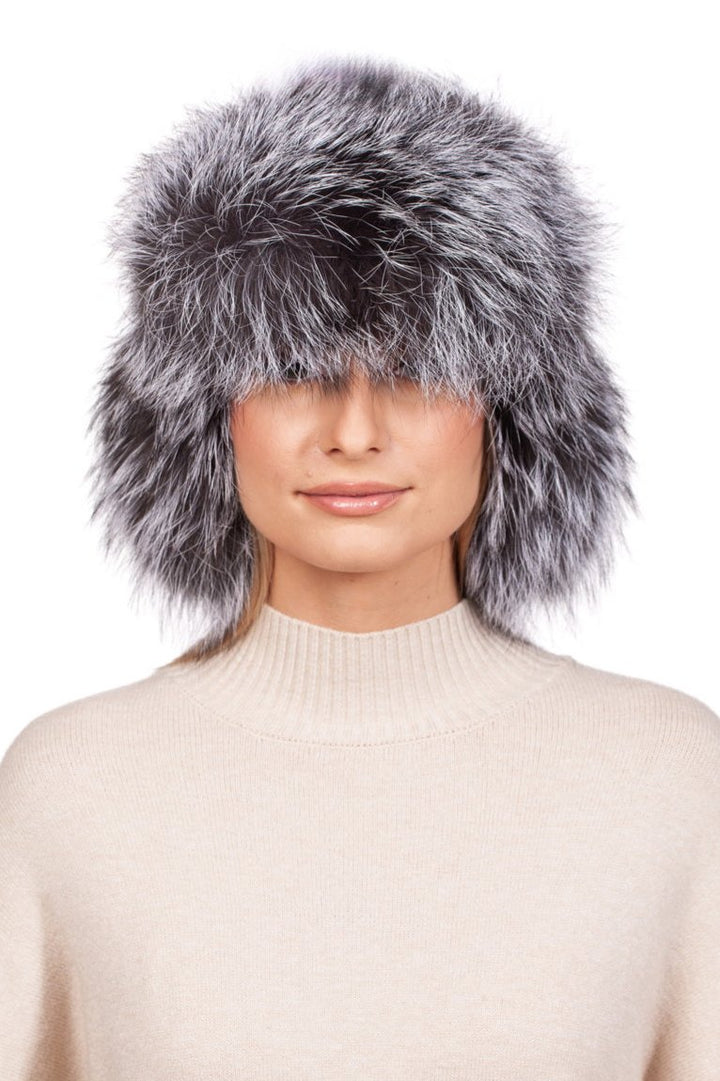 A person wearing the Silver Fox Fur Ushanka Trapper Hat by FurbySD, crafted from fluffy gray fur that partially covers their face, is paired with a cream-colored sweater. The white background highlights the texture and elegance of this luxurious winter accessory.