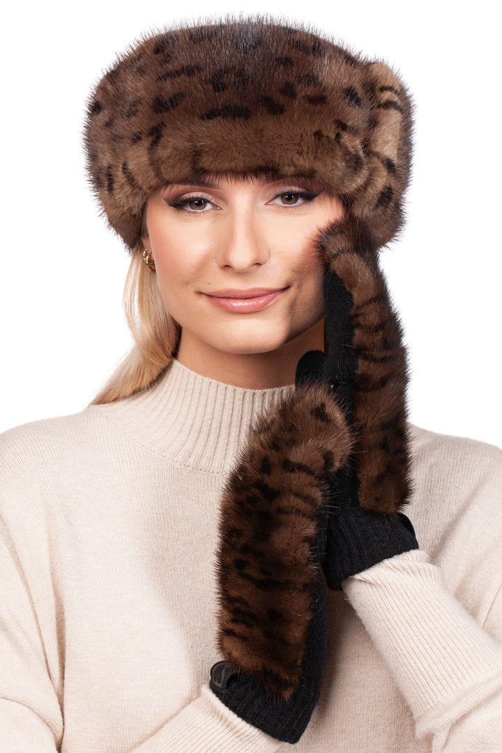 Wearing a beige sweater, a person adds a stylish touch to their look with the Leopard Print Fur Headband and Mittens by FurbySD. They smile slightly, gently touching the side of their face against the pristine white background.