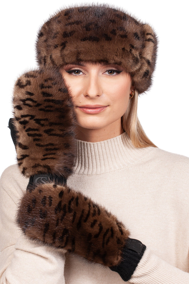 A woman dressed in a beige turtleneck sweater, wearing a FurbySD Leopard Print Fur Headband and Mittens, has long blonde hair and is striking a pose with one hand lifted to her face while looking at the camera.