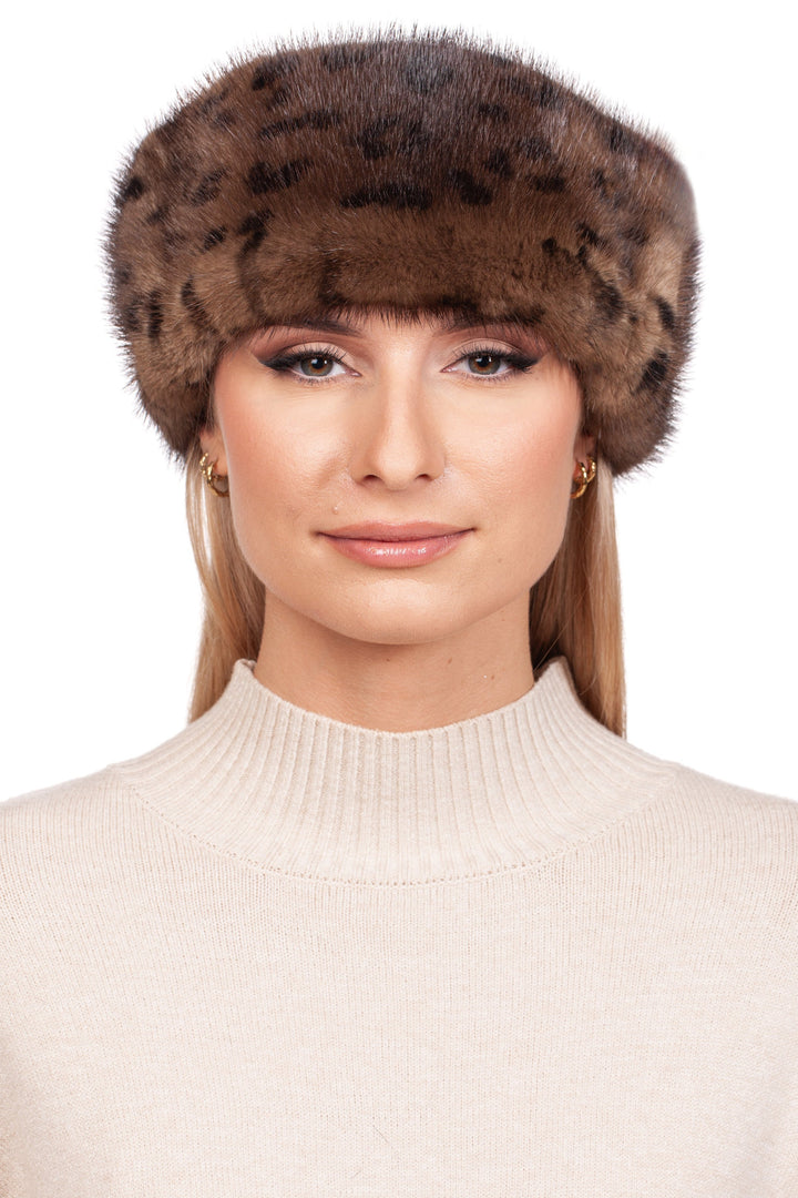 A person wearing a beige sweater is adorned with the Leopard Print Mink Fur Headband by FurbySD. The plain white background accentuates the chic fashion and accessories.