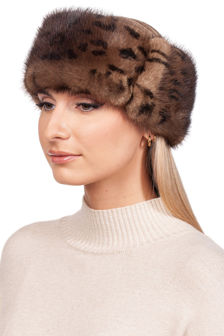 A woman wearing a luxurious FurbySD Leopard Print Mink Fur Headband and a cream turtleneck sweater has long blonde hair and is gazing to the left. Her expression remains calm, accentuated by small hoop earrings, against a plain white background.