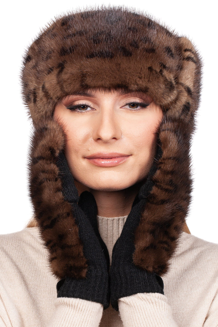 A person wearing a FurbySD Leopard Print Fur Headband and Mittens holds the sides of the headband against their cheeks. They are dressed in a cream-colored sweater against a plain white background.