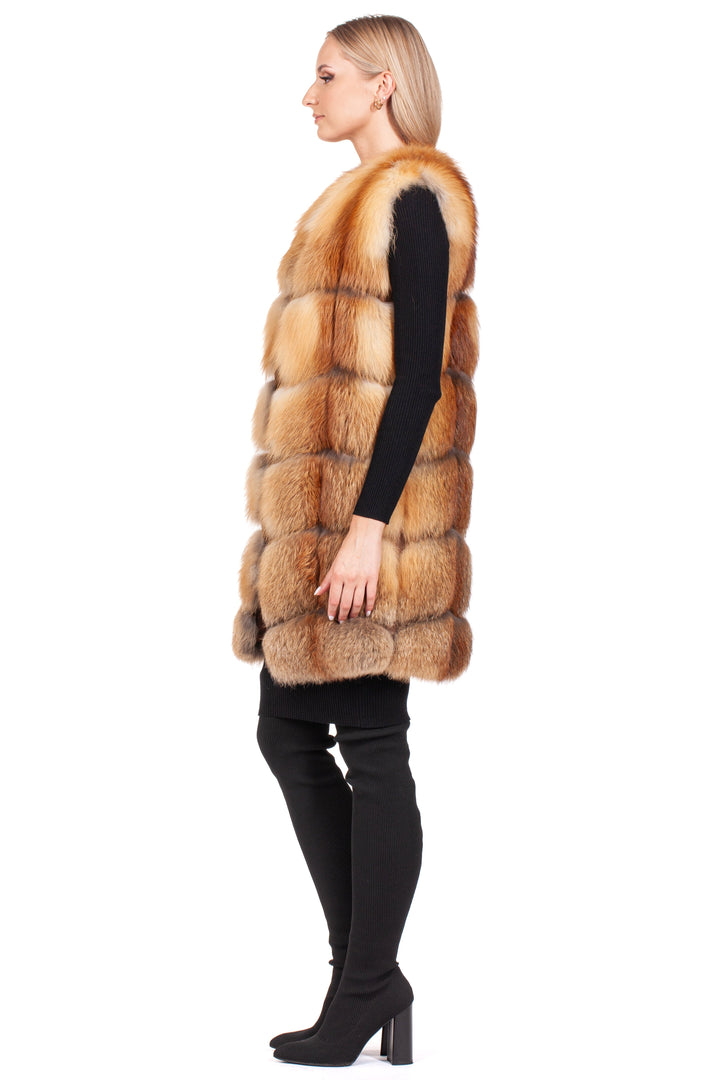 A blonde woman in profile showcases an elegant winter ensemble, highlighted by a Long Red Fox Fur Vest from FurbySD layered over her black attire, all set against a clean white backdrop.