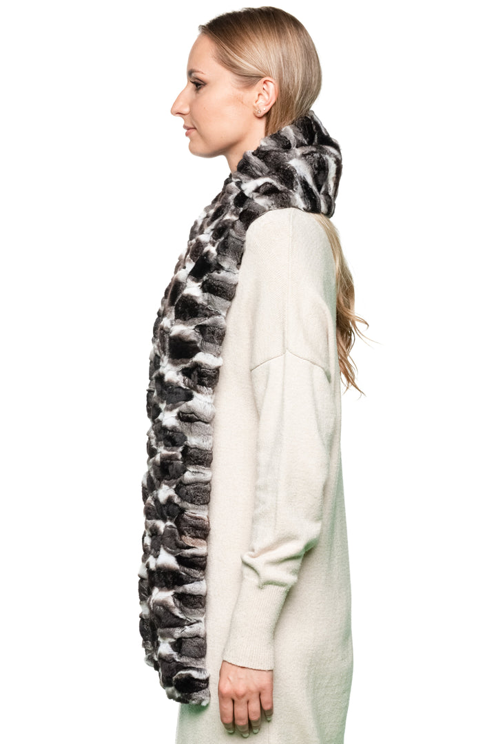 Woman wearing a long, light-colored coat with a black and white patterned  chinchilla fur scarf.
