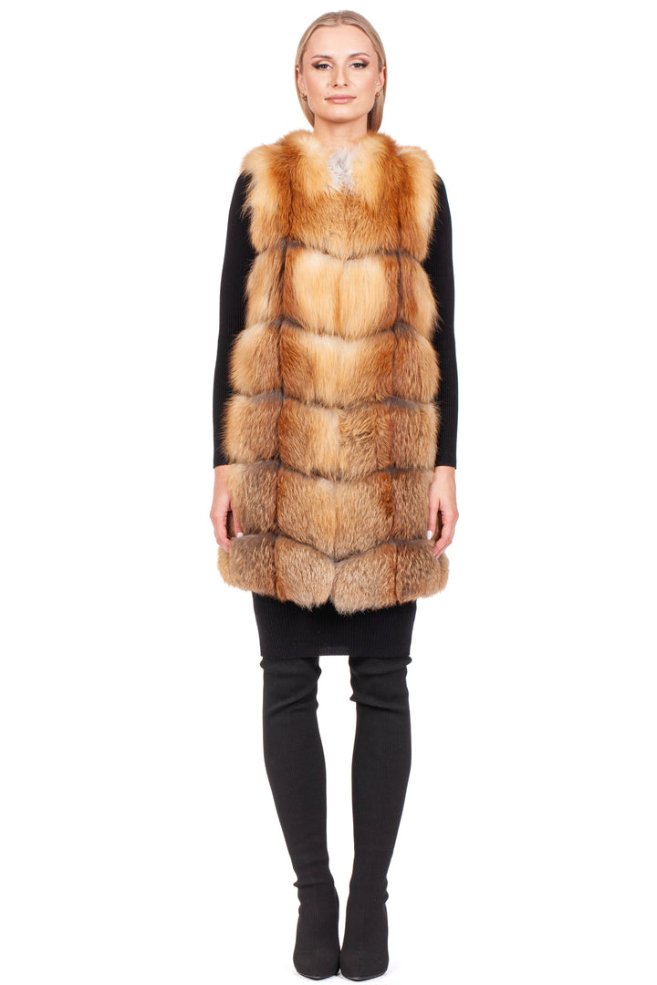 A person is elegantly dressed in a sophisticated winter ensemble, highlighted by the luxurious Long Red Fox Fur Vest from FurbySD. This quilted vest in reddish-brown and beige tones complements a sleek black outfit featuring long sleeves, pants, and boots, all set against a white backdrop for an exquisite display.