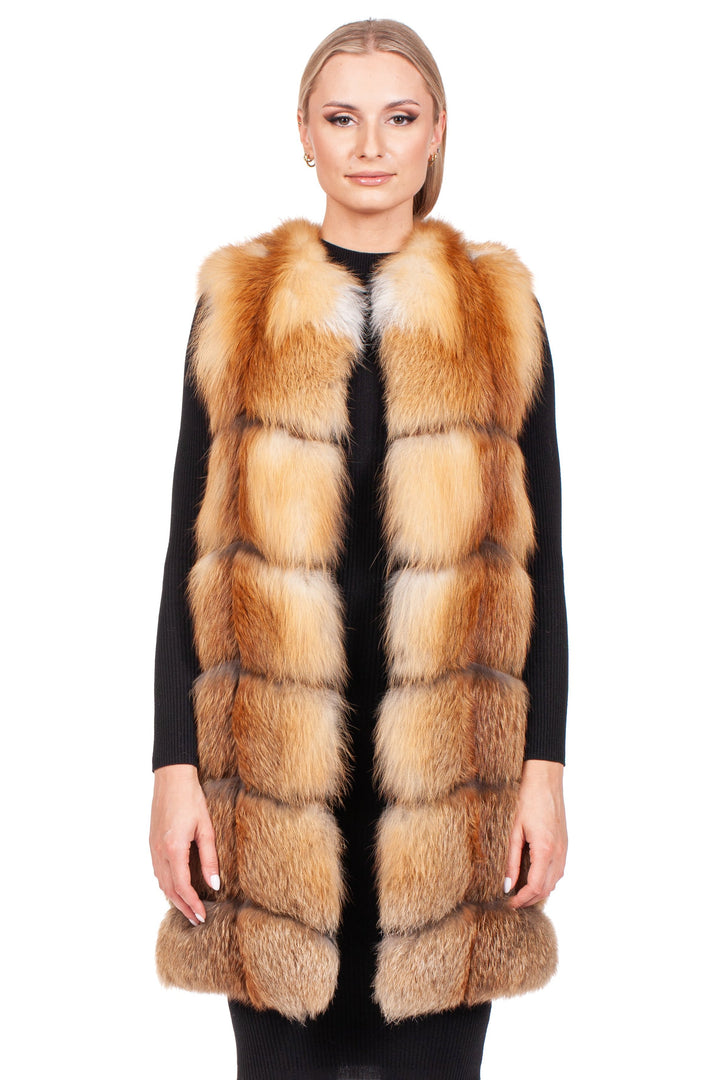 A person stands facing forward, displaying a sophisticated winter wardrobe featuring the Long Red Fox Fur Vest by FurbySD over a black outfit. The luxurious, reddish-brown hue of the sleeveless vest contrasts elegantly against the plain white background.