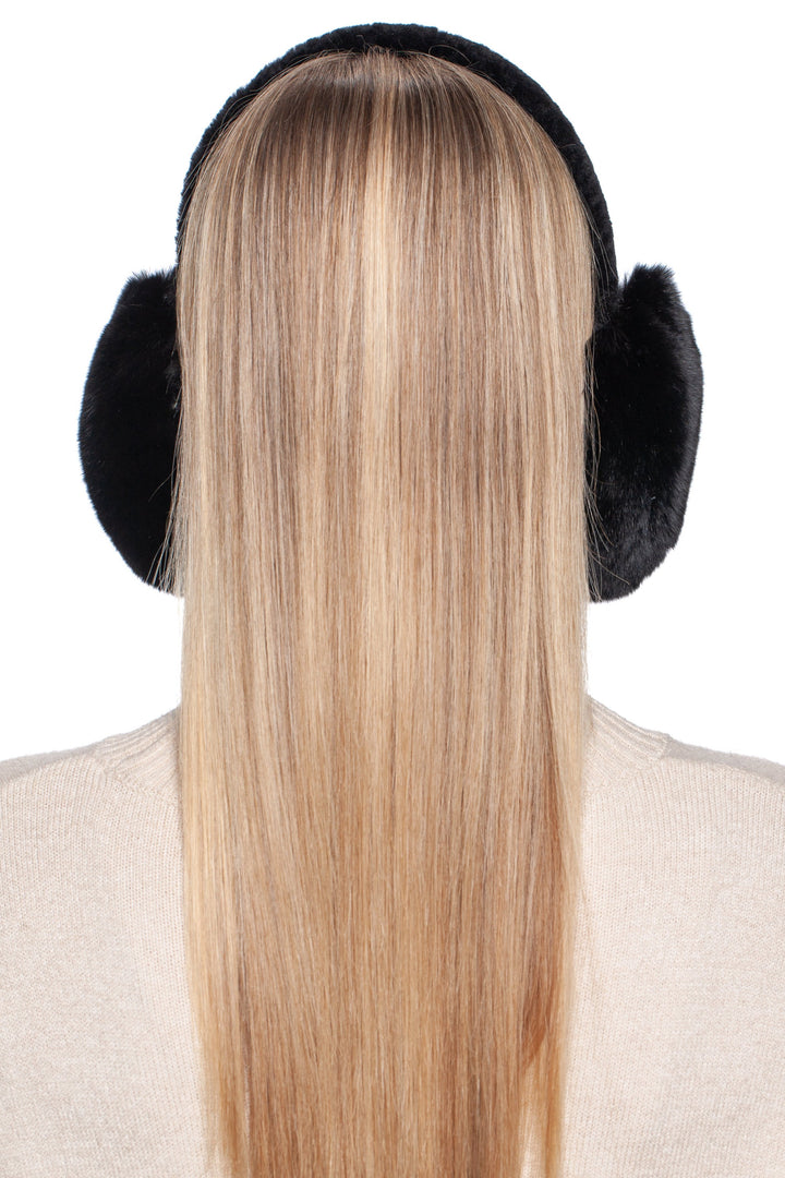 A person with long, straight blonde hair is seen from behind, wearing FurbySD's stylish Black Chinchilla Fur Earmuffs with an Astrakhan Band, paired with a beige sweater, all set against a plain white background.