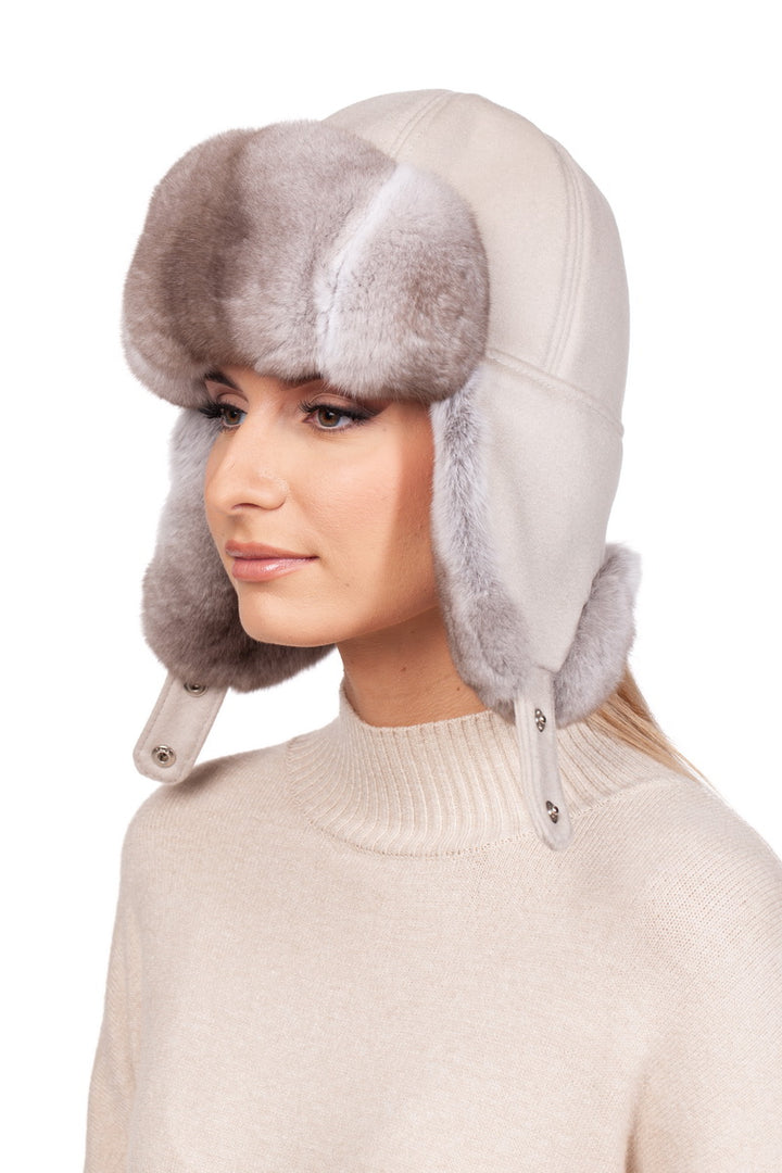 A woman wearing a cream white turtleneck sweater and a beige chinchilla fur ushanka hat featuring earflaps.