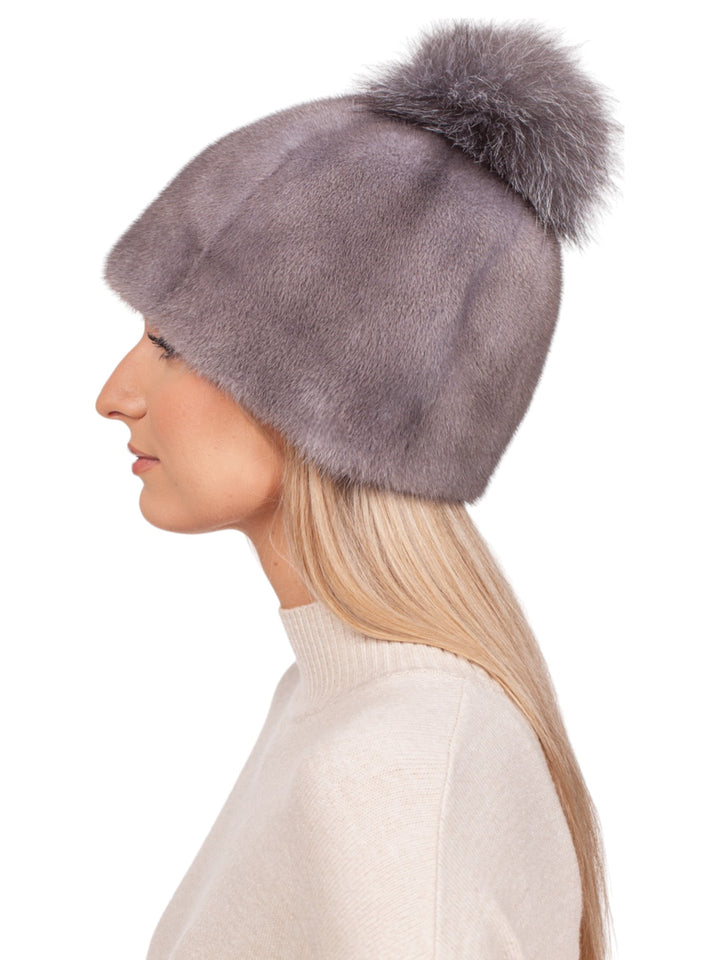 A person with long blonde hair is wearing a luxurious Silver Blue Mink Fur Hat With a fluffy fox pom-pom by FurbySD. They are dressed in a light beige sweater and are looking to the left against a plain white background.