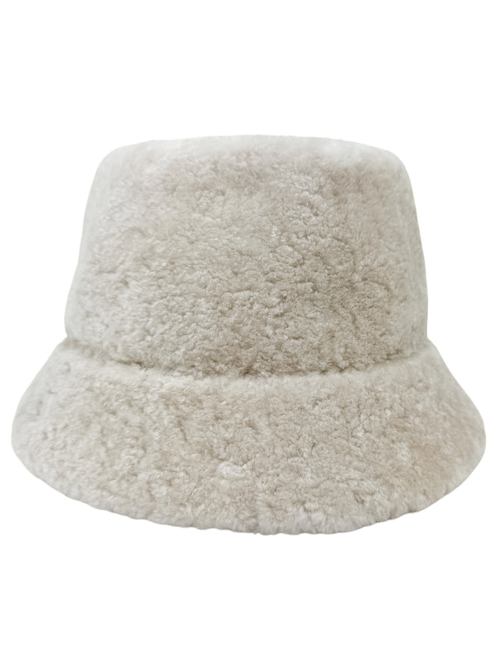 Featured on a plain white background, the Pearl White Astrakhan Fur Bucket Hat by FurbySD is a light beige, fluffy accessory with an exceptionally soft texture.