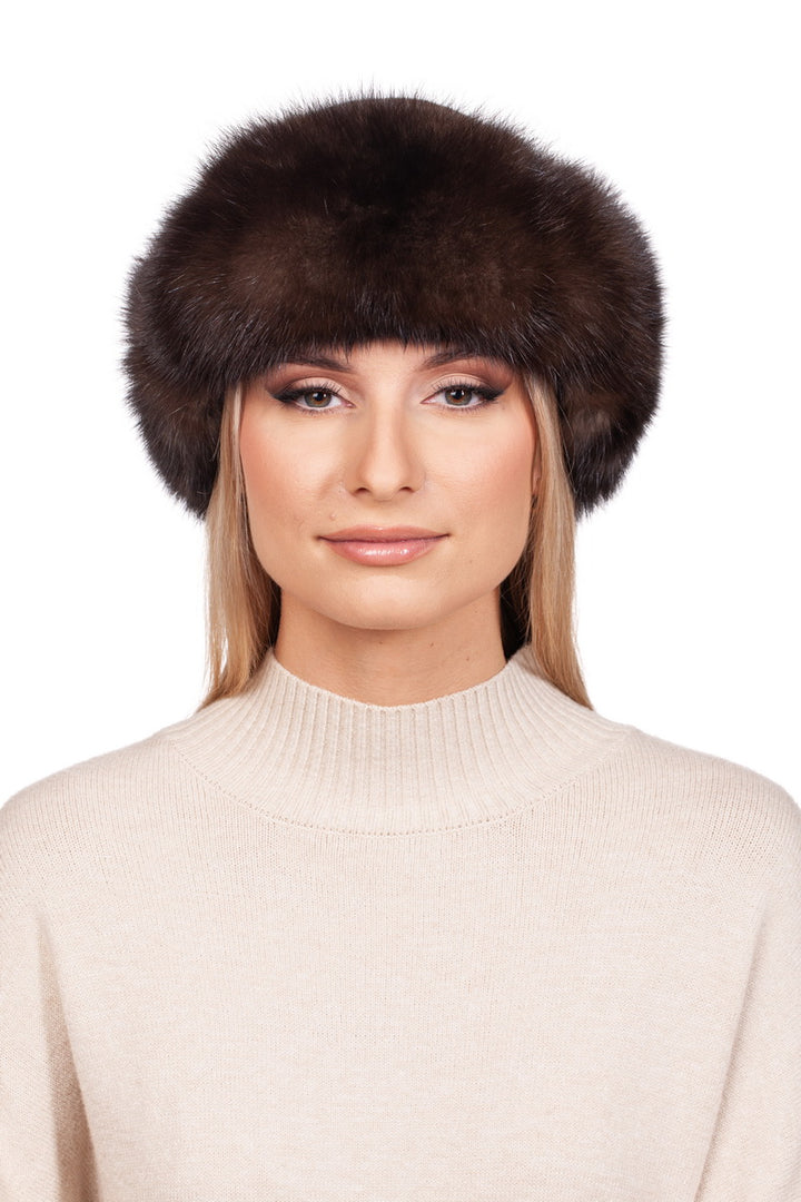 A person wearing a fluffy, dark brown Barguzin sable fur ushanka hat from FurbySD and a light beige sweater stands against a white background. They have long, blonde hair and subtle makeup with a neutral expression.