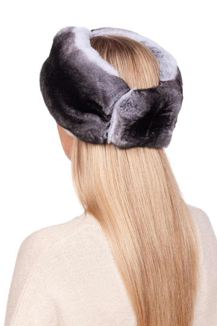 A person with long blonde hair sports a luxurious accessory: the Twisted Chinchilla Fur Headband in dark gray by FurbySD. Wearing a light beige top, they pose against a plain white background. The winter style headband elegantly covers the top of their head and is visible from behind.