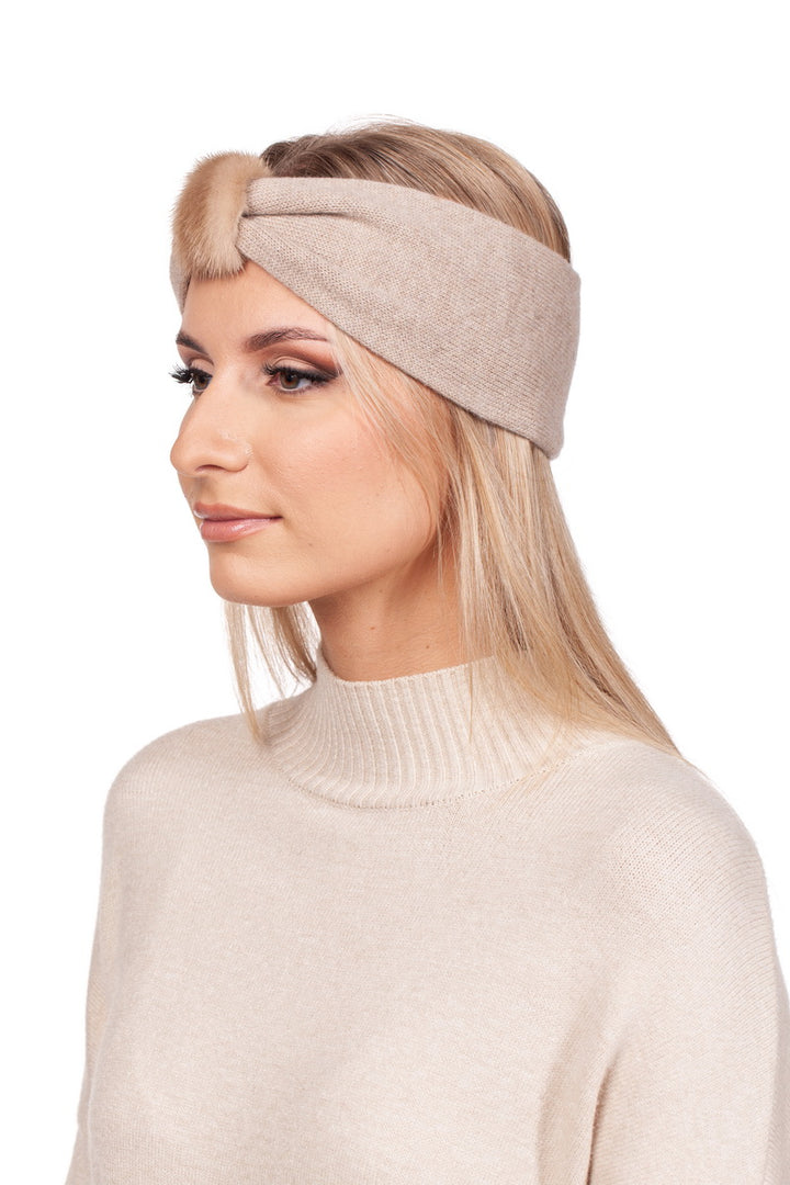 A woman elegantly poses against a plain white background, wearing a FurbySD Beige Mink Fur and Cashmere Headband, adorned with a luxurious faux fur knot, and perfectly paired with a matching high-neck sweater.